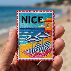 May include: A rectangular embroidered patch shaped like a postage stamp with a scalloped red border. The design features a beach scene with the word NICE in black letters, two blue and white striped umbrellas, lounge chairs, and a building.
