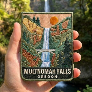 May include: A rectangular embroidered patch featuring a landscape of Multnomah Falls in Oregon. The design includes a white waterfall, a stone bridge, green pine trees, rocky cliffs, and an orange sun against a peach sky. The text reads MULTNOMAH FALLS OREGON.