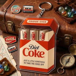 May include: A quirky Diet Coke-themed keychain, designed to resemble a cigarette box, with three tiny cans inside. The box is red and white, with the words "Diet Coke" and "Fridge Cigs". Other items include pins, a compass, marbles, and a vintage suitcase.