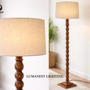 May include: A wooden floor lamp with a beige linen shade. The lamp has a dark brown, turned wood base and a square base. The text "LumaNest Lighting" is visible on the image.