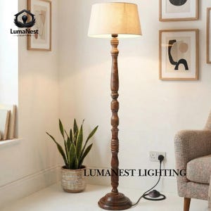 May include: A tall, wooden floor lamp with a beige lampshade. The lamp has a dark brown, turned wood base and stem. The lamp is plugged into a wall outlet. The text "LumaNest Lighting" is visible at the bottom of the image.