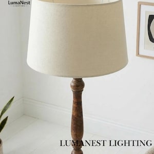May include: A tall floor lamp with a beige fabric shade and a dark brown wooden base. The lamp has a classic design and is suitable for living rooms or bedrooms. The text "LumaNest Lighting" is visible at the bottom of the lamp.