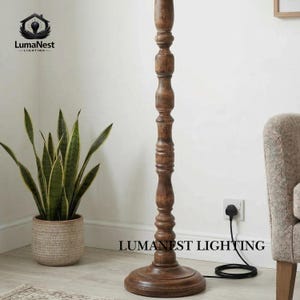 May include: A tall, wooden floor lamp with a dark brown finish. The lamp has a turned, decorative column and a round base. A potted snake plant sits to the left of the lamp. The text "LumaNest Lighting" is at the bottom.