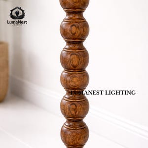May include: A close-up of a wooden lamp post with a turned design. The post is a warm brown color and has a series of rounded sections. The text "LumaNest Lighting" is visible in the image.