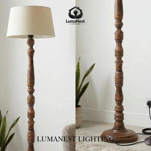 May include: A wooden floor lamp with a beige lampshade. The lamp has a dark brown, carved wooden base and pole. The lamp is plugged into a wall outlet. The lamp is next to a potted plant.