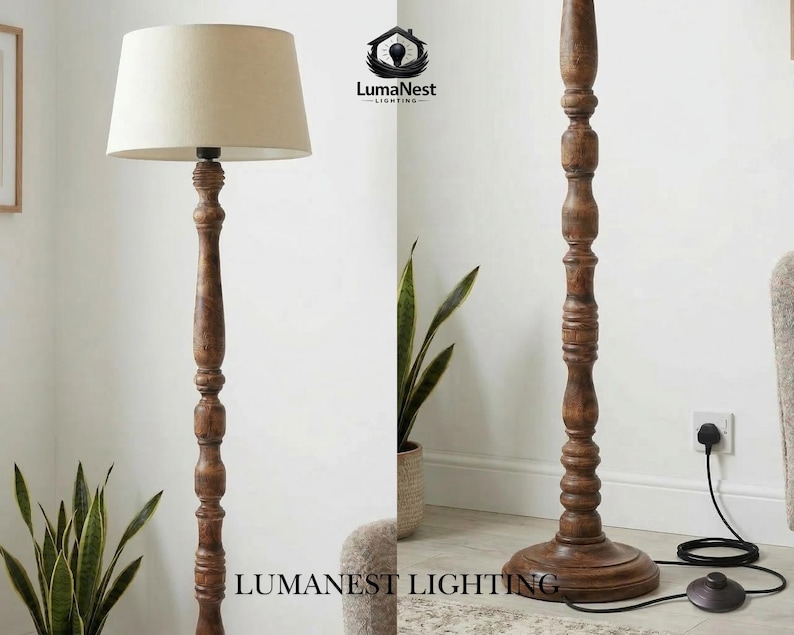 May include: A wooden floor lamp with a beige lampshade. The lamp has a dark brown, carved wooden base and pole. The lamp is plugged into a wall outlet. The lamp is next to a potted plant.