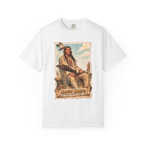 Könnte beinhalten: Ein weißes kurzärmeliges T-Shirt mit einem Grafikdruck einer indianischen Figur mit langem Haar und Federschmuck. Der Text lautet CRAZY HORSE OGLALA LAKOTA TRIBE. Die Illustration zeigt eine Person in traditioneller Kleidung.