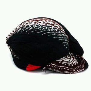 Puede incluir: Un sombrero negro con patrones blancos y marrones y un acento rojo. El sombrero presenta un diseño distintivo con patrones blancos y marrones sobre un fondo negro. El sombrero está hecho de un material suave y es adecuado para diversas ocasiones.