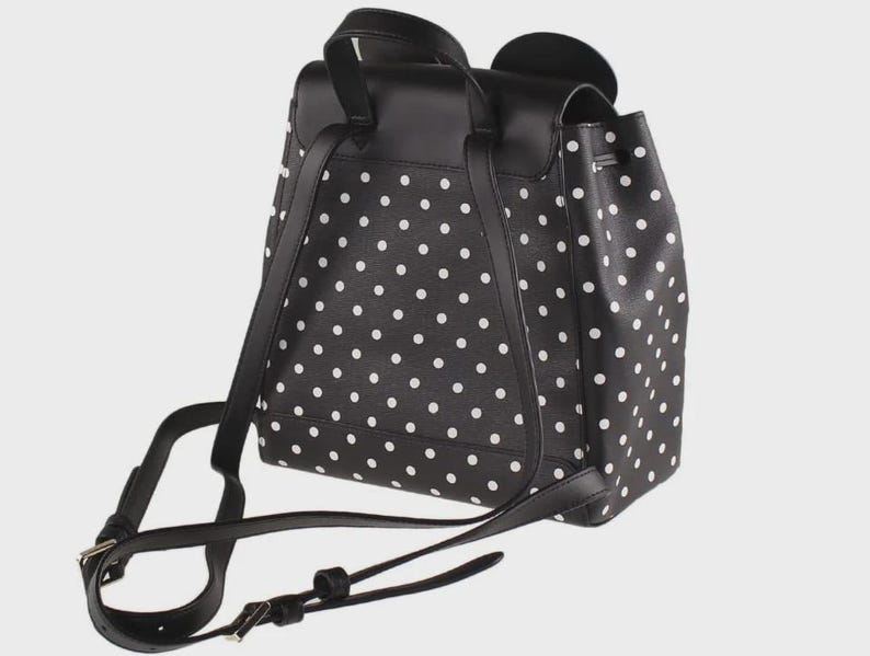 May include: Black backpack with white polka dots. The backpack has adjustable straps and a top handle. The bag features a flap closure and a drawstring closure. The backpack is made of a durable material.