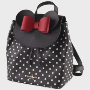 May include: Black backpack with white polka dots, featuring a black flap with a red bow and mouse ears. The bag has a drawstring closure and a top handle. The brand name "kate spade new york" is visible on the front.