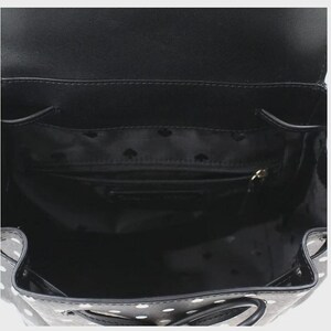 May include: Black backpack with white polka dots, open to reveal the interior. The interior is black with a small zippered pocket and a lining with a repeating spade pattern. The bag has a drawstring closure and a flap.