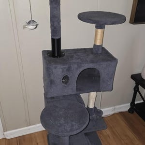 May include: A multi-level cat tree in shades of gray, featuring multiple platforms, a hideaway cubby, and scratching posts. A dangling toy hangs from the top level. The cat tree is designed for feline entertainment and relaxation.