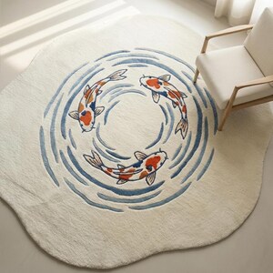 May include: A round, off-white rug featuring a koi pond design. Three koi fish in orange, white, and black swim in a circle within blue water lines. The rug has a soft, textured appearance and a unique, irregular edge.
