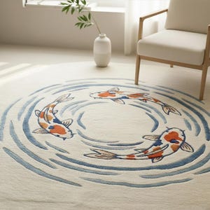 May include: A round, off-white rug featuring three koi fish in shades of orange, white, and blue, swimming in a circular pattern of blue water lines. The rug is placed on a light-colored floor.