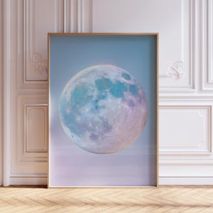 Pode incluir: Uma impressão emoldurada com uma grande lua colorida. A lua é retratada em tons de azul, verde-azulado e roxo, contra um céu azul claro. A obra de arte é exibida em uma moldura de madeira, adicionando calor à cena celestial.
