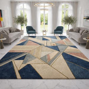 May include: A large geometric rug in a living room setting. The rug features a pattern of triangles and lines in navy blue, beige, light blue, and pink. The rug is placed in front of two blue armchairs and two grey sofas. The room has large windows.
