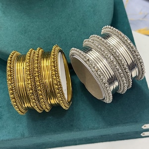 Pode incluir: Dois conjuntos de pulseiras empilhadas, um em tom dourado polido e outro em tom prateado polido. Cada conjunto consiste em várias bandas finas e lisas intercaladas com bandas texturizadas com contas que apresentam um padrão de pontos.