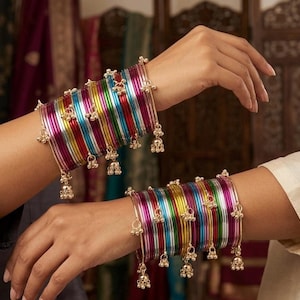 Può includere: Un set di braccialetti rigidi in metallo multicolore nelle tonalità magenta, giallo, verde e blu, con finitura lucida. La serie comprende diversi braccialetti sottili decorati con piccoli campanellini dorati pendenti sui bordi esterni.
