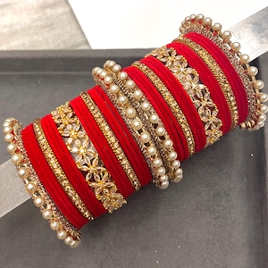 May include: A stack of red velvet bangles interspersed with gold-toned metal bands featuring clear rhinestones and white faux pearls. A metal ruler is visible through the center, showing the stack measures approximately 6.4 cm in diameter.