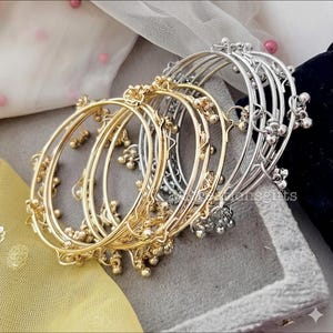 Peut inclure: Plusieurs bracelets de cheville dorés et argentés. Les bracelets sont ornés de petits grelots suspendus. Les bracelets dorés ont une finition chaude et brillante, tandis que les bracelets argentés ont un aspect brillant et poli. Les bracelets sont empilés.