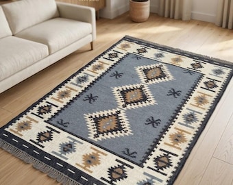 May include: Handwoven wool Kilim rug with a geometric design. The rug features a central field of blue with diamond and star patterns in brown, white, and gray. A border of white, brown, and blue geometric shapes surrounds the central field.