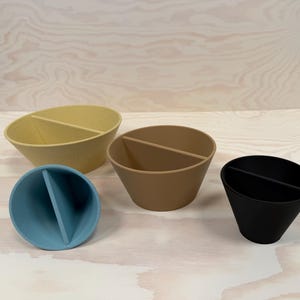 May include: Four divided containers in light yellow, brown, blue, and black. Each has a single divider, creating two compartments. The containers are arranged on a light wood-grain surface.