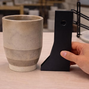 May include: A set of three ceramic mugs with a speckled, matte finish in cream, light grey, and dark grey. Each mug has a simple, minimalist design and a rounded handle.