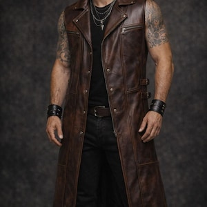 May include: A brown leather vest with a longline design. The vest features a notched collar, a zip pocket, and button closures. It has a tailored fit and is worn over a black shirt and jeans. The vest has a vintage, distressed look.
