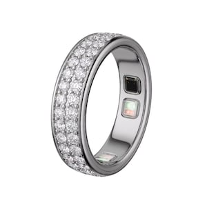 Può includere: Un anello d'argento con due file di piccole pietre preziose trasparenti. L'anello ha una fascia liscia e lucida e presenta due piccoli sensori quadrati sulla superficie interna. L'anello è progettato per essere indossato su un dito.