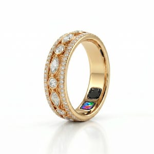 May include: A gold ring featuring a central band set with alternating marquise and round cut clear stones, bordered by two rows of small pavé-set stones. The inner surface of the band displays a black square sensor and a small iridescent square.