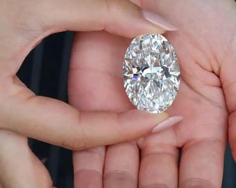 May include: A large, clear, oval-cut gemstone with numerous facets that reflect light, creating a brilliant, sparkling appearance. The stone is colorless and transparent, showcasing a high level of clarity and precision cutting throughout its surface.