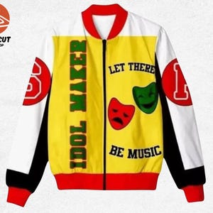 May include: A zip-up bomber jacket featuring a yellow front panel with the text IDOL MAKER and LET THERE BE MUSIC, accompanied by red and green theatrical masks. The sleeves are white with black side panels and red cuffs, collar, and hem.