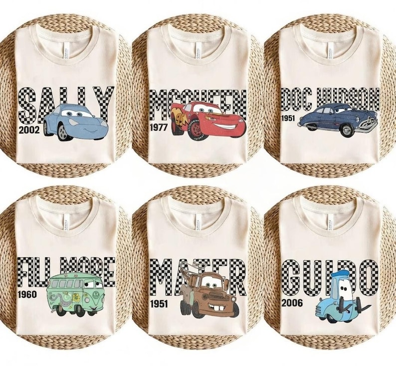 May include: Six cream-coloured t-shirts featuring cartoon car characters. Each shirt has a different car name in a black and white chequered font, with the car's image and a year. The cars include Sally, McQueen, Doc Hudson, Fillmore, Mater, and Guido.