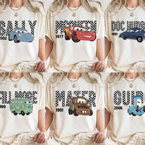 May include: Cream-coloured t-shirts featuring cartoon car characters from the film Cars. Each shirt has a different character name in a checkered font, with the year the character was introduced.