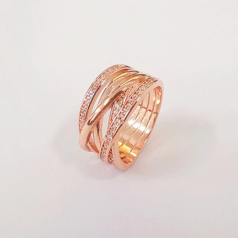 Puede incluir: Anillo de oro rosa con un dise&ntilde;o multibanda. El anillo presenta bandas entrelazadas, algunas de las cuales est&aacute;n incrustadas con peque&ntilde;os cristales brillantes. El dise&ntilde;o general es elegante y moderno, adecuado para el uso diario u ocasiones especiales.
