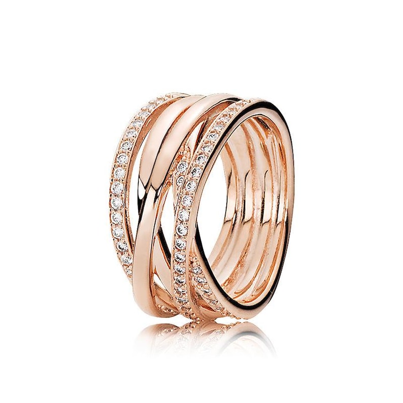 Puede incluir: Anillo de oro rosa con bandas entrelazadas. Una banda est&aacute; incrustada con peque&ntilde;os cristales transparentes. El anillo tiene un acabado pulido y un dise&ntilde;o moderno. El anillo se muestra sobre un fondo blanco.