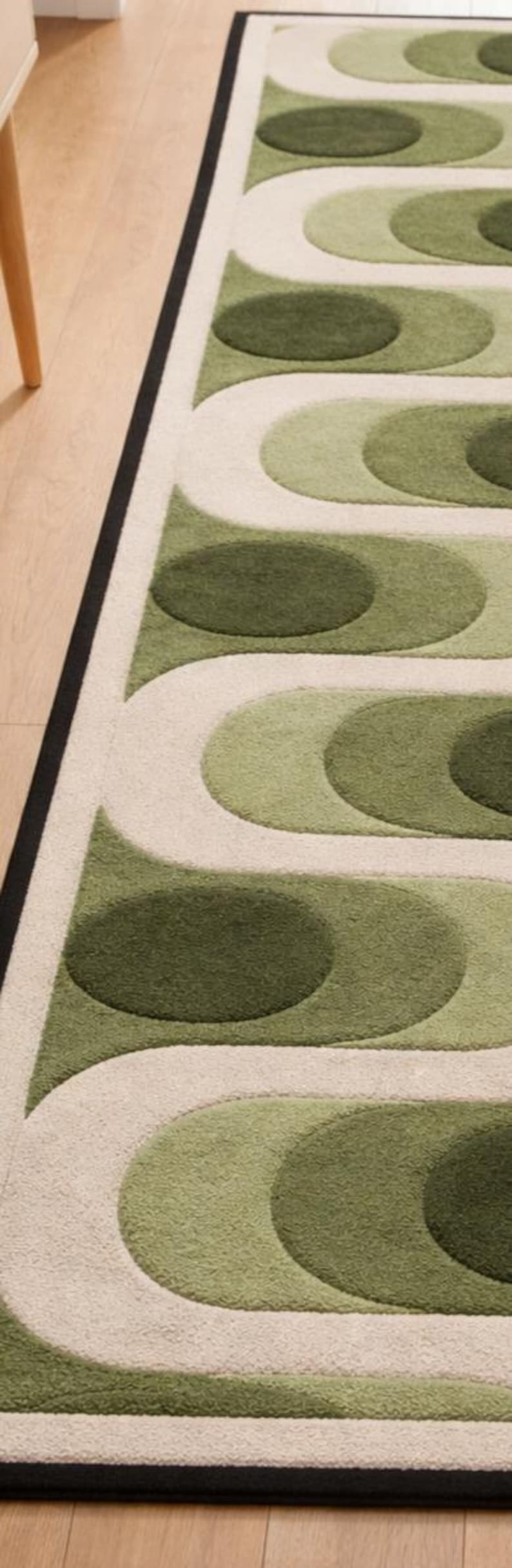 Puede incluir: Una alfombra estampada en verde y blanco roto con un borde negro. La alfombra presenta un dise&ntilde;o repetitivo de l&iacute;neas curvas y formas ovaladas en diferentes tonos de verde. La alfombra est&aacute; sobre un suelo de madera.