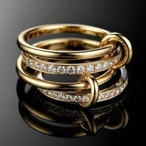 May include: A stack of three gold rings with a unique design. The top and bottom rings are plain gold, while the middle ring is adorned with a row of small, sparkling diamonds. The rings are interlocked with a knot-like feature.