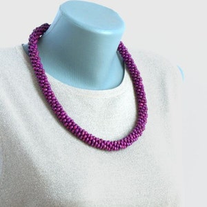 May include: A purple beaded necklace made of small, round beads. The necklace is on a white mannequin.