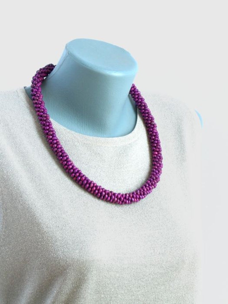 May include: A purple beaded necklace made of small, round beads. The necklace is on a white mannequin.