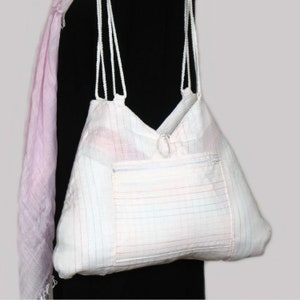 May include: White tote bag with a zippered pocket and thin white straps. The bag is made of a white fabric with thin red, blue, and pink stripes.