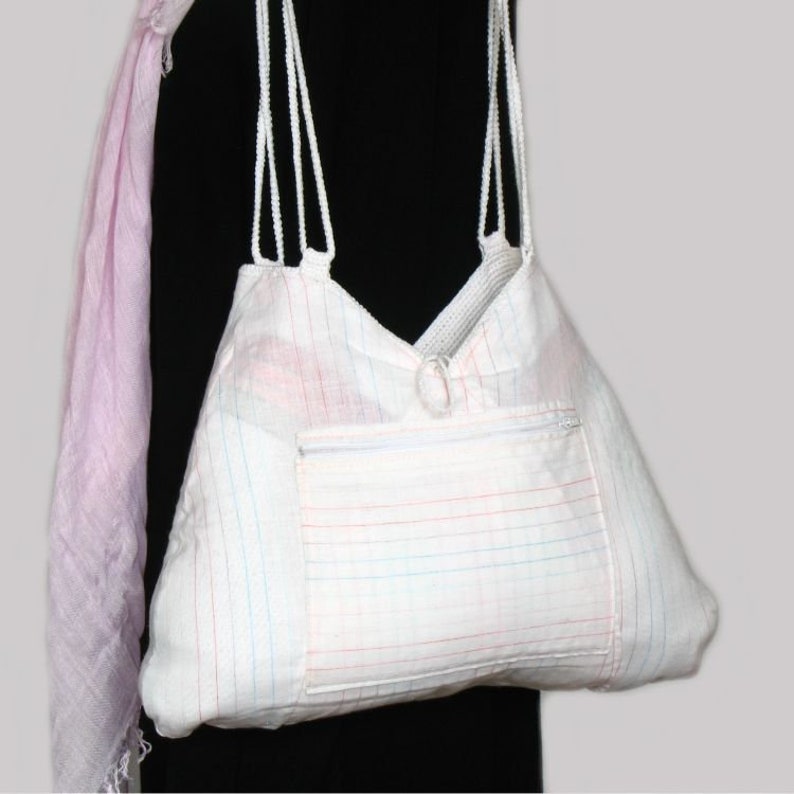 May include: White tote bag with a zippered pocket and thin white straps. The bag is made of a white fabric with thin red, blue, and pink stripes.