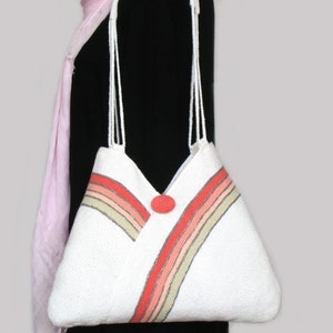 May include: White crocheted tote bag with a red button and multi-colored stripes. The bag has a long strap.