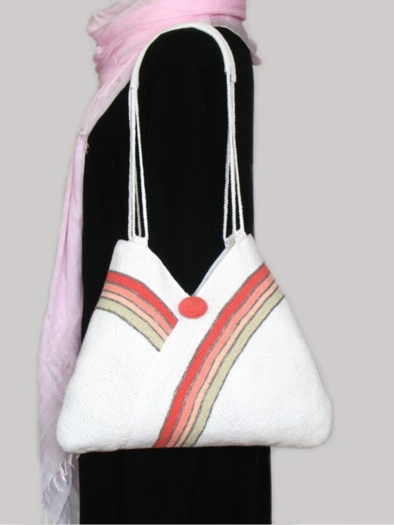 May include: White crocheted tote bag with a red button and multi-colored stripes. The bag has a long strap.