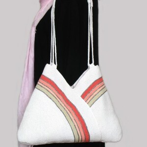 May include: White crocheted tote bag with a multi-colored stripe design. The stripe is made of pink, orange, and beige yarn.