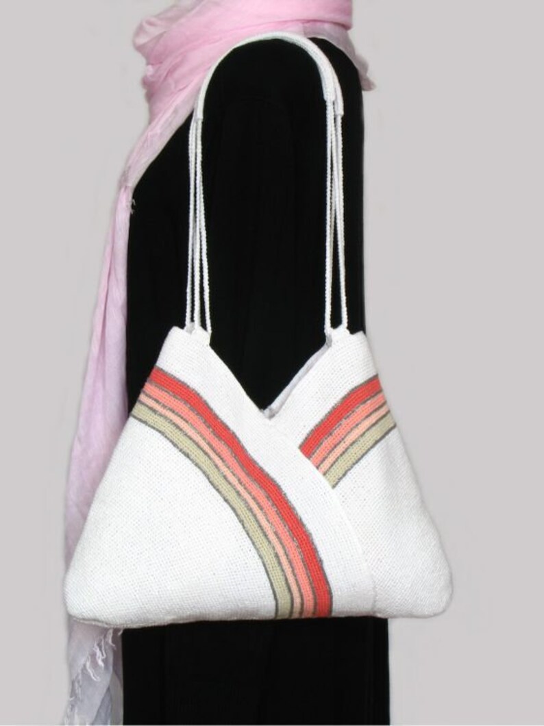 May include: White crocheted tote bag with a multi-colored stripe design. The stripe is made of pink, orange, and beige yarn.