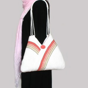 May include: White tote bag with a red, pink, and beige striped design. The bag has a single button closure and two white straps.