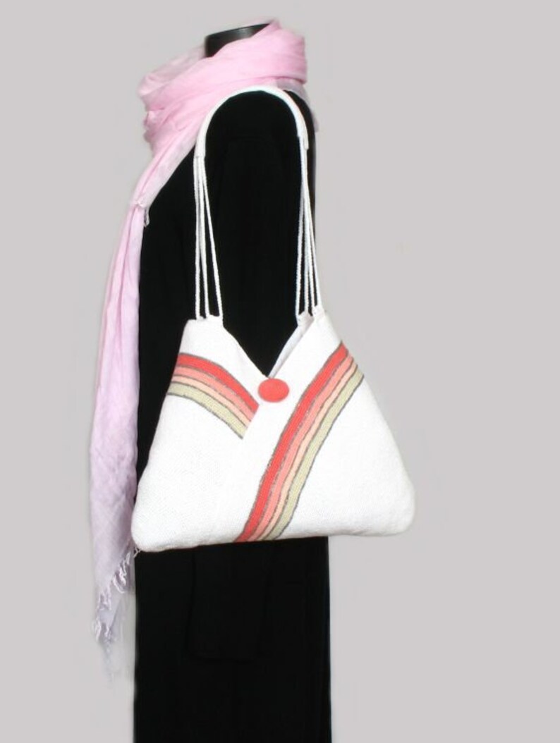 May include: White tote bag with a red, pink, and beige striped design. The bag has a single button closure and two white straps.