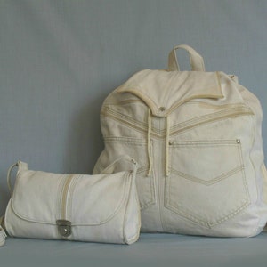 Puede incluir: Dos bolsos de lona de color blanco roto. Una mochila grande con cierre de cordón y un bolso bandolera más pequeño con cierre de plata. Ambos bolsos tienen un patrón texturizado sutil.