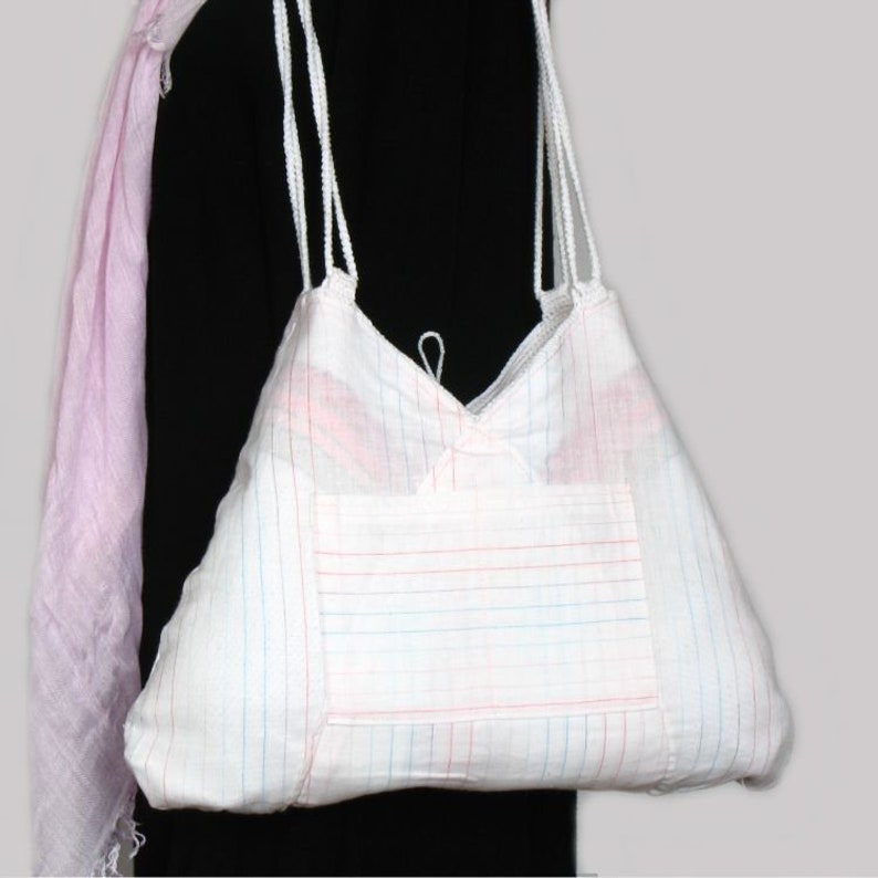 May include: A white tote bag with a large pocket on the front. The bag is made of striped fabric with red, blue, and white stripes. The bag has a pink lining.